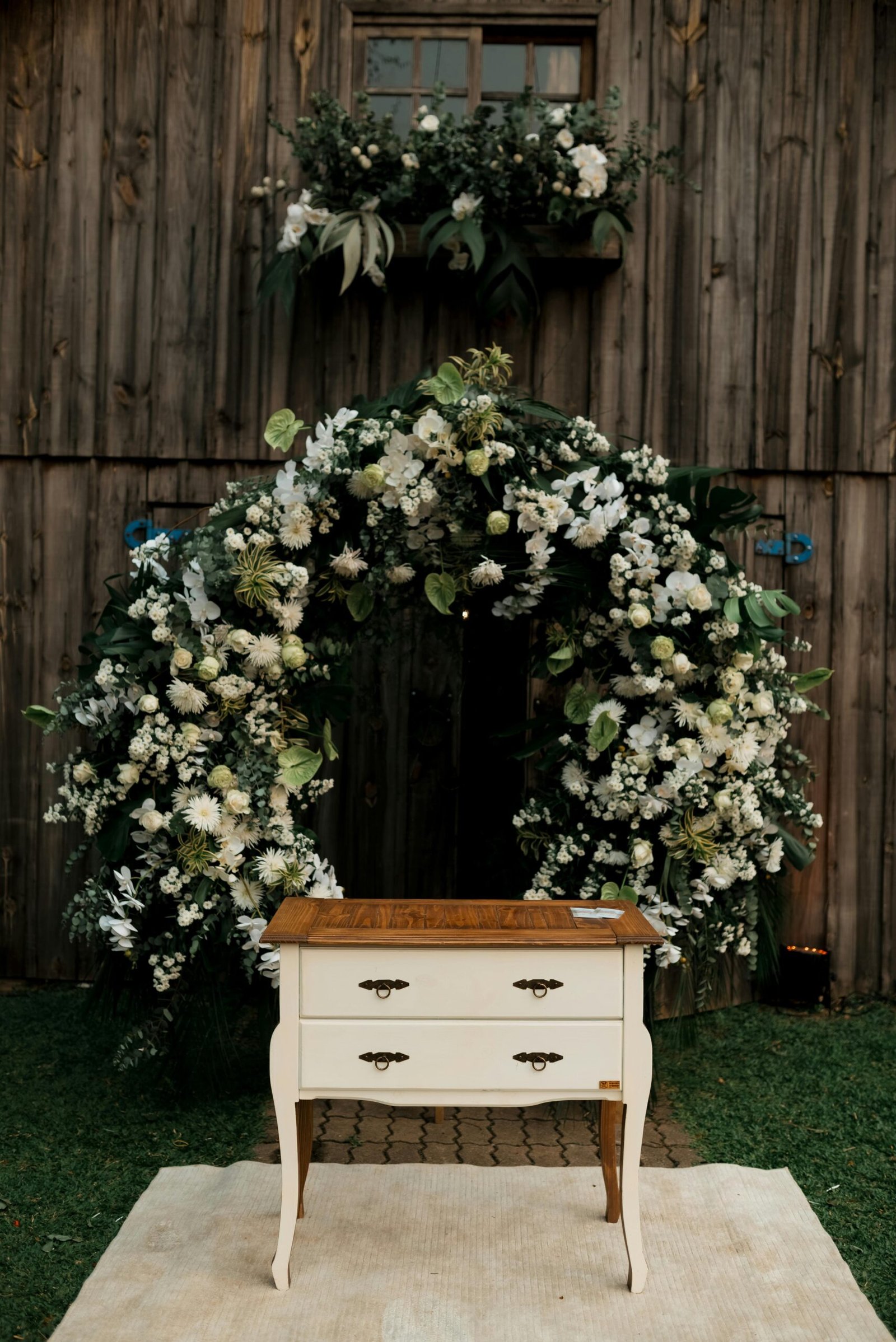 Charming rustic wedding scene with flower arch and wooden dresser.